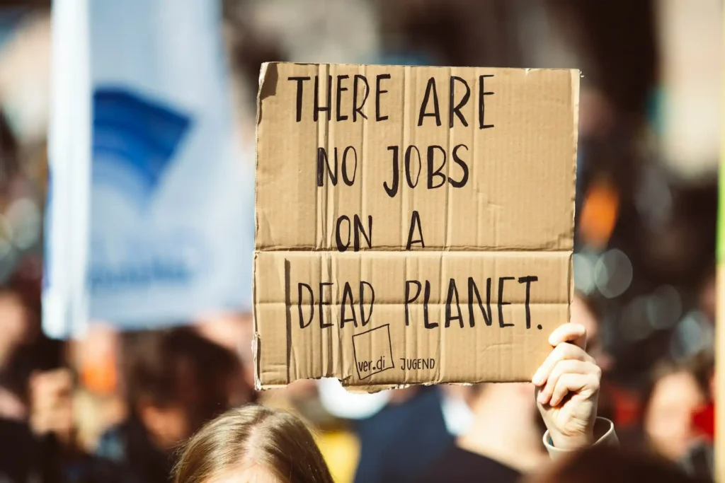 Un gruppo di manifestanti in una piazza affollata, ognuno con un cartello con slogan scritti a mano contro il cambiamento climatico e per la protezione ambientale.