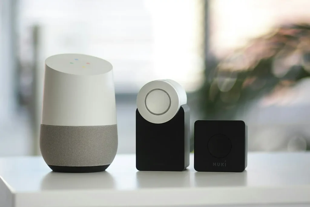 Una collezione di dispositivi smart home, inclusi un termostato intelligente, un hub di controllo cilindrico, e una telecamera di sicurezza, disposti su una scrivania in un ambiente domestico contemporaneo.
