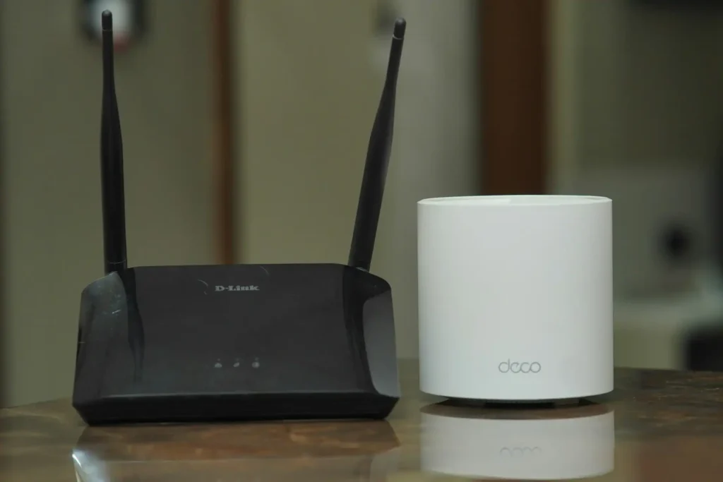 Un vecchio modello D-link di router Wi-Fi con antenne esterne, posto su un mobile in legno, che rappresenta uno dei primi passi verso la tecnologia smart home.