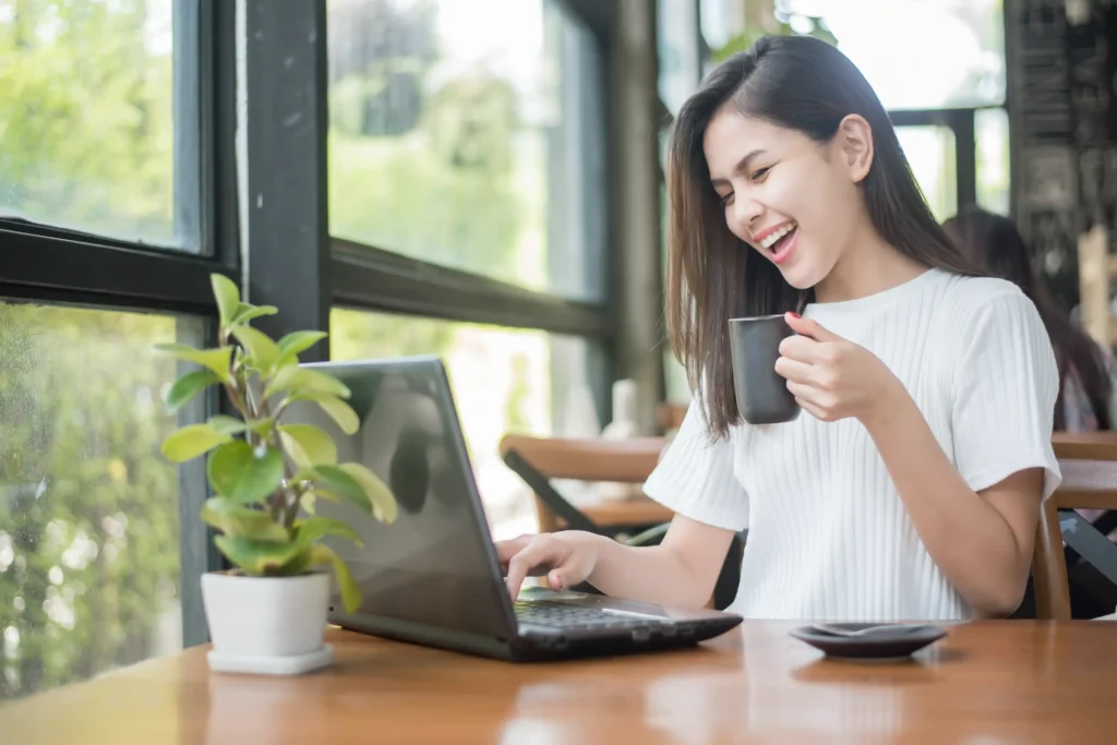 Una ragazza sorridente seduta a casa davanti al suo laptop, felice mentre naviga su internet.